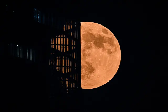 Një hënë me ngjyrë të kuqe pas një rrokaqielli natën.