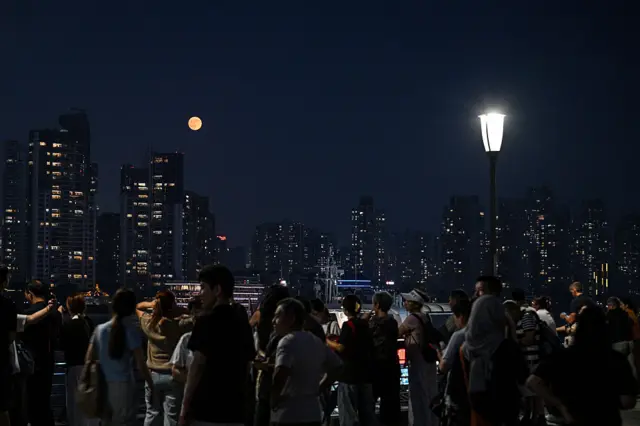 Njerëzit mblidhen në një shëtitore, përpara pamjes së rrokaqiejve, ndërsa një Hënë e Përgjakur lind në qiellin e natës.